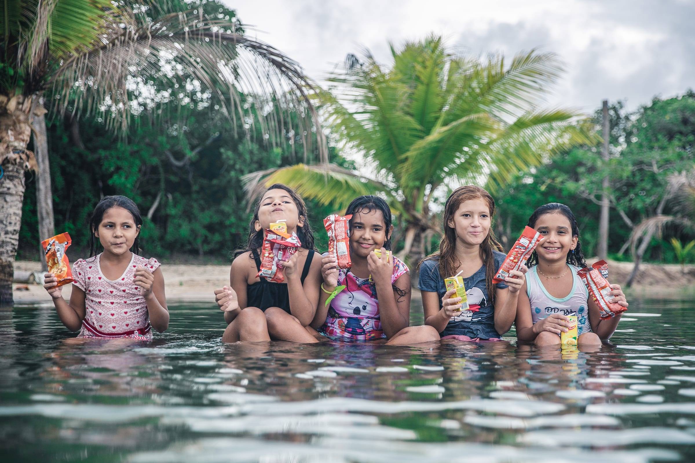 Girls laugh together while sitting in a lake with snacks