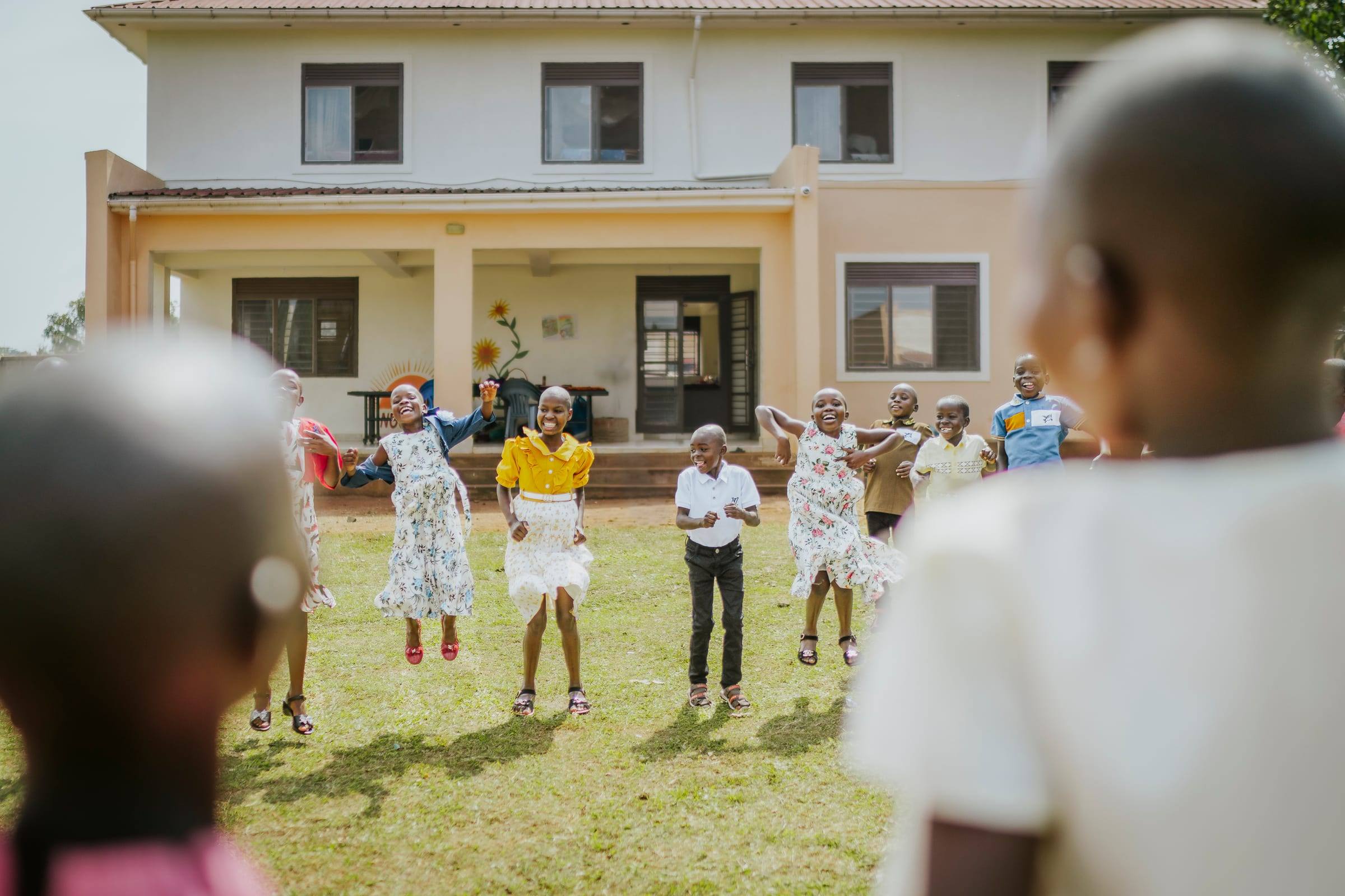 Children dance together on the lawn in front of a school