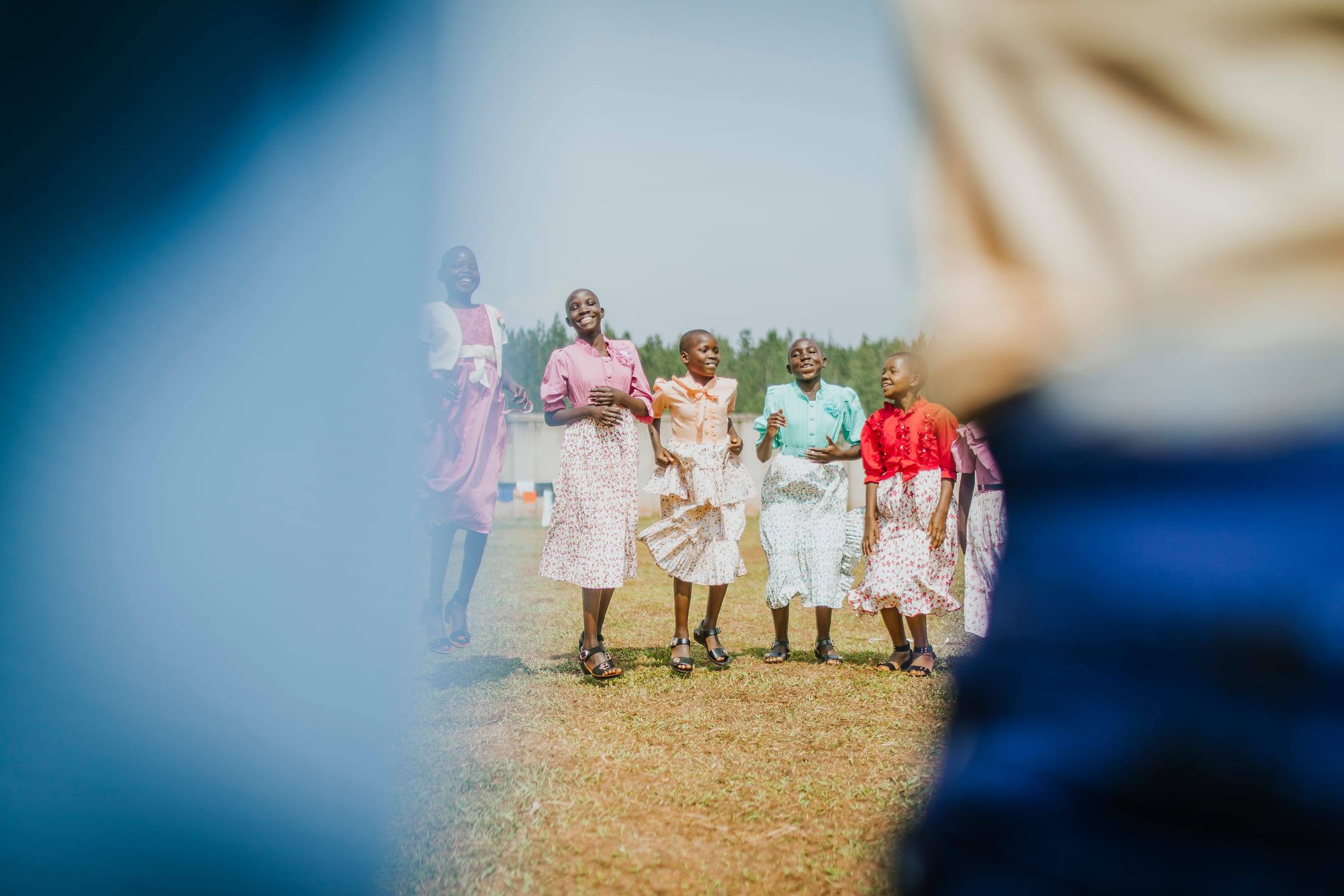 Women in white dresses dance together on a lawn by the water