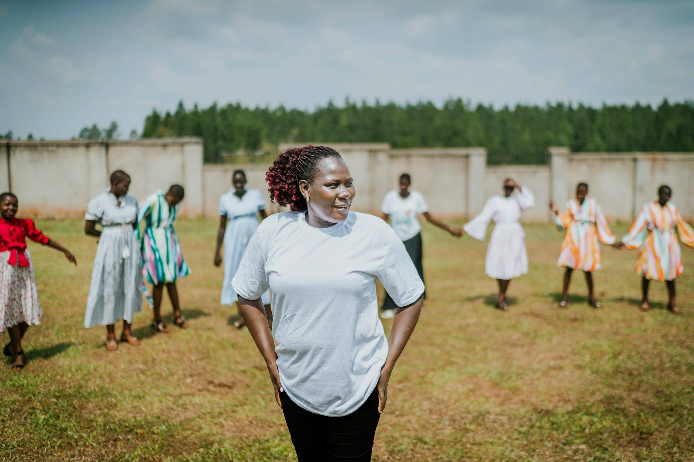 A local leader smiles in a school field while women and girls dance behind her