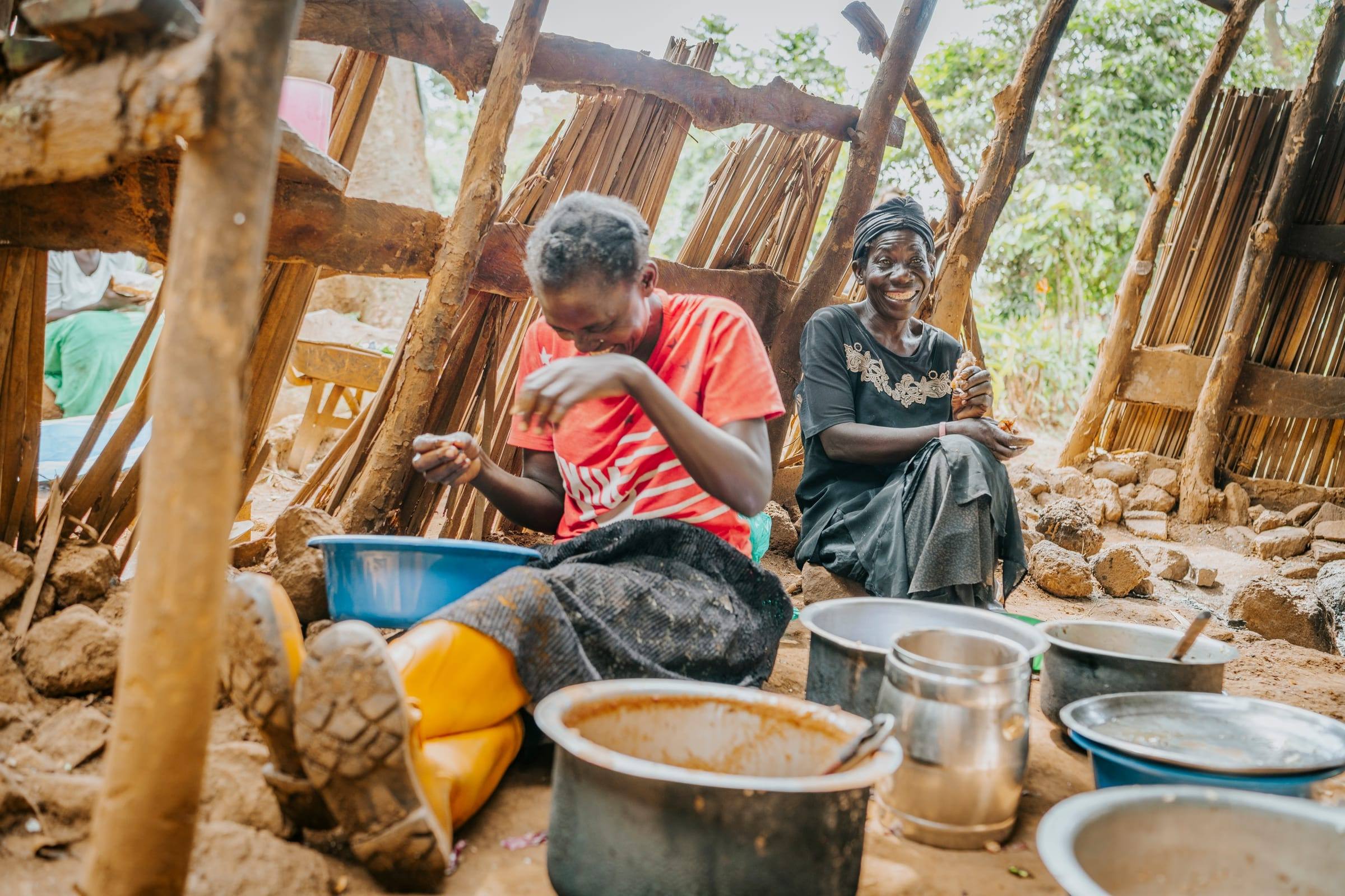 Two women laugh as they cook together in an outdoor kitchen