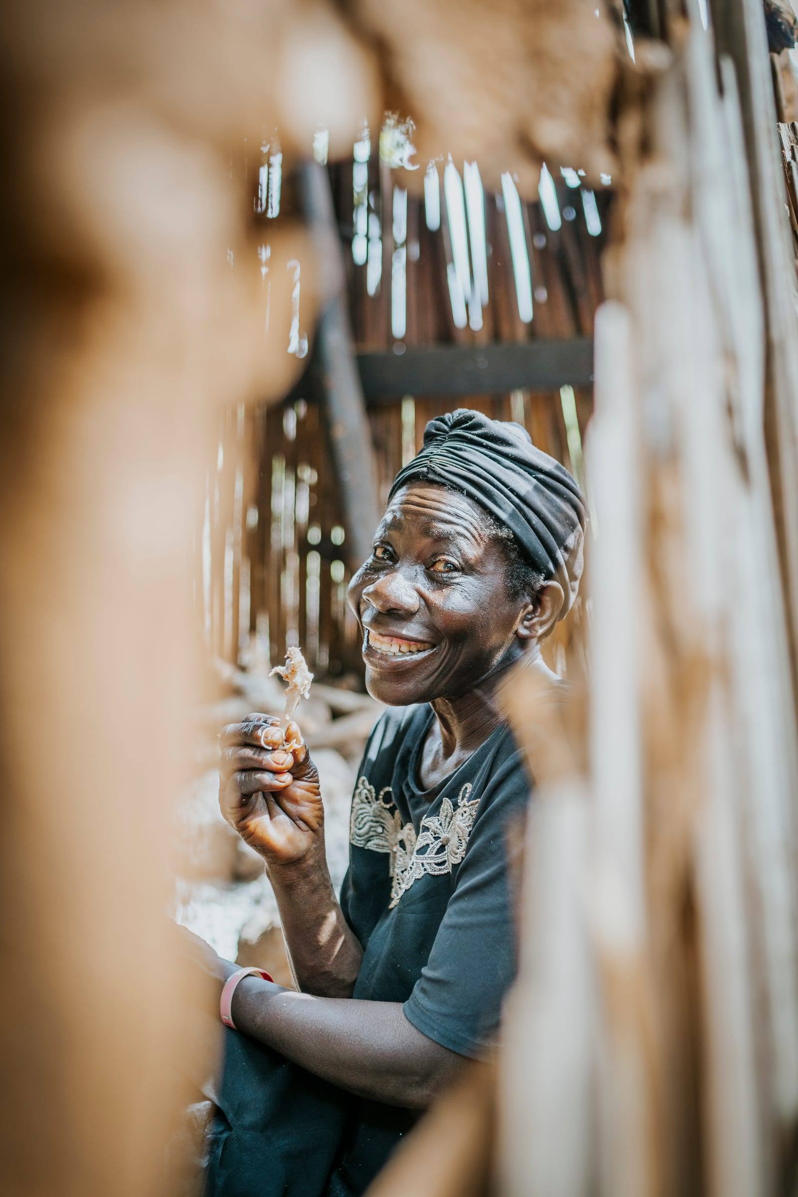 A woman in a headwrap smiles broadly beside a doorway