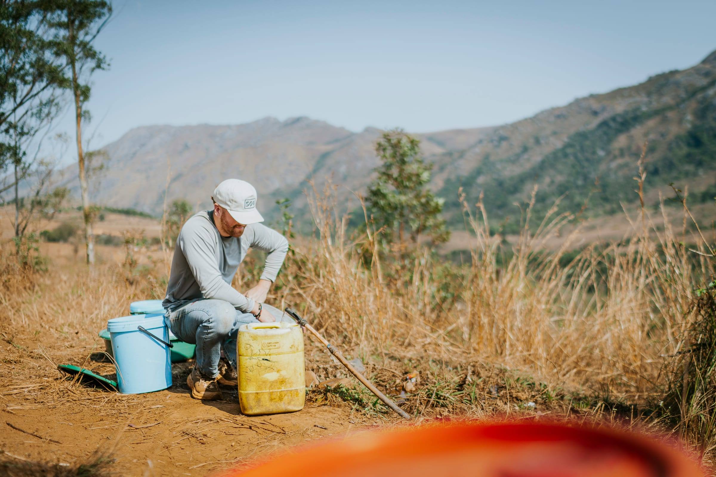 A volunteer fills water containers on a dry hillside outside Manzini