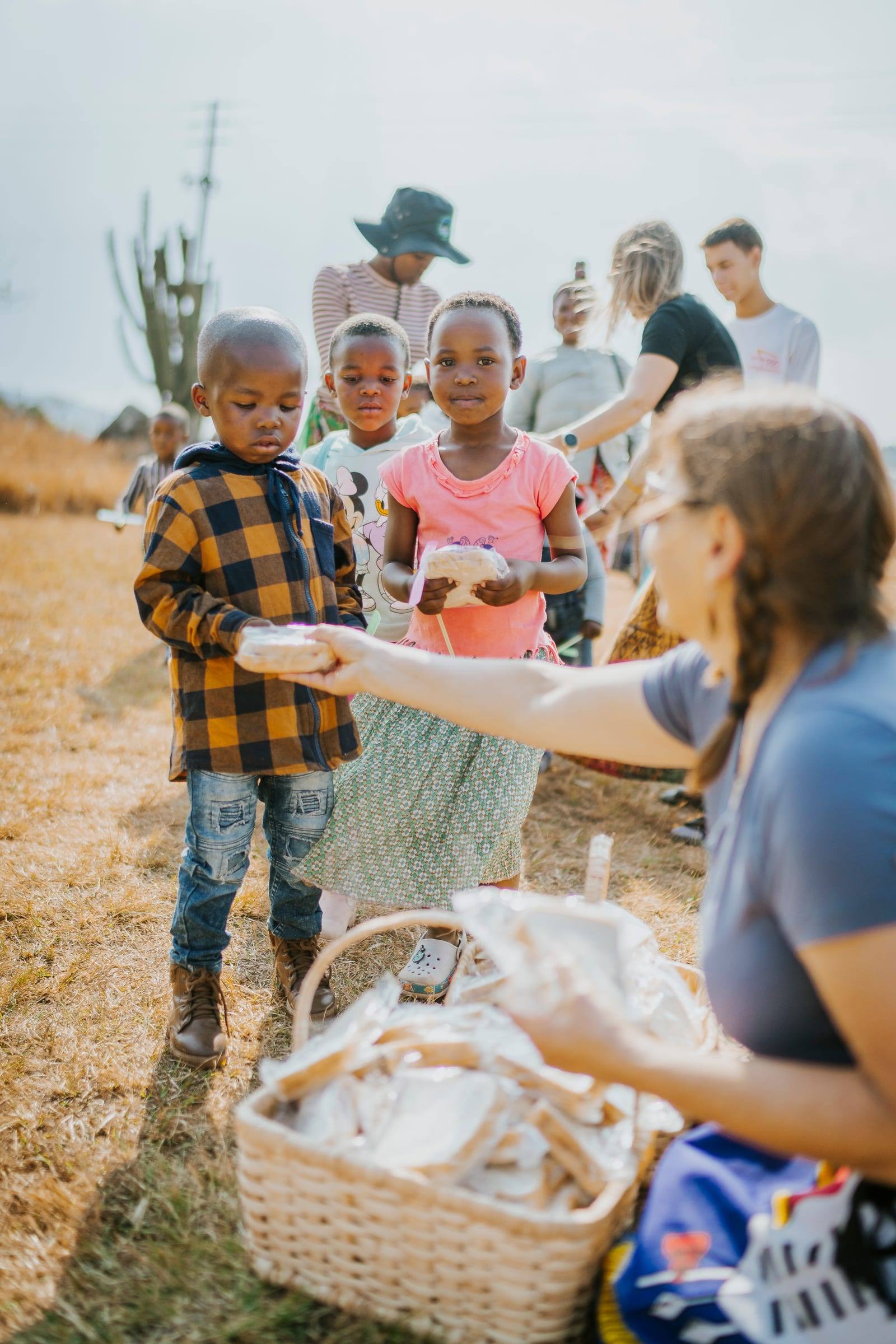 A volunteer hands snacks to a line of smiling children