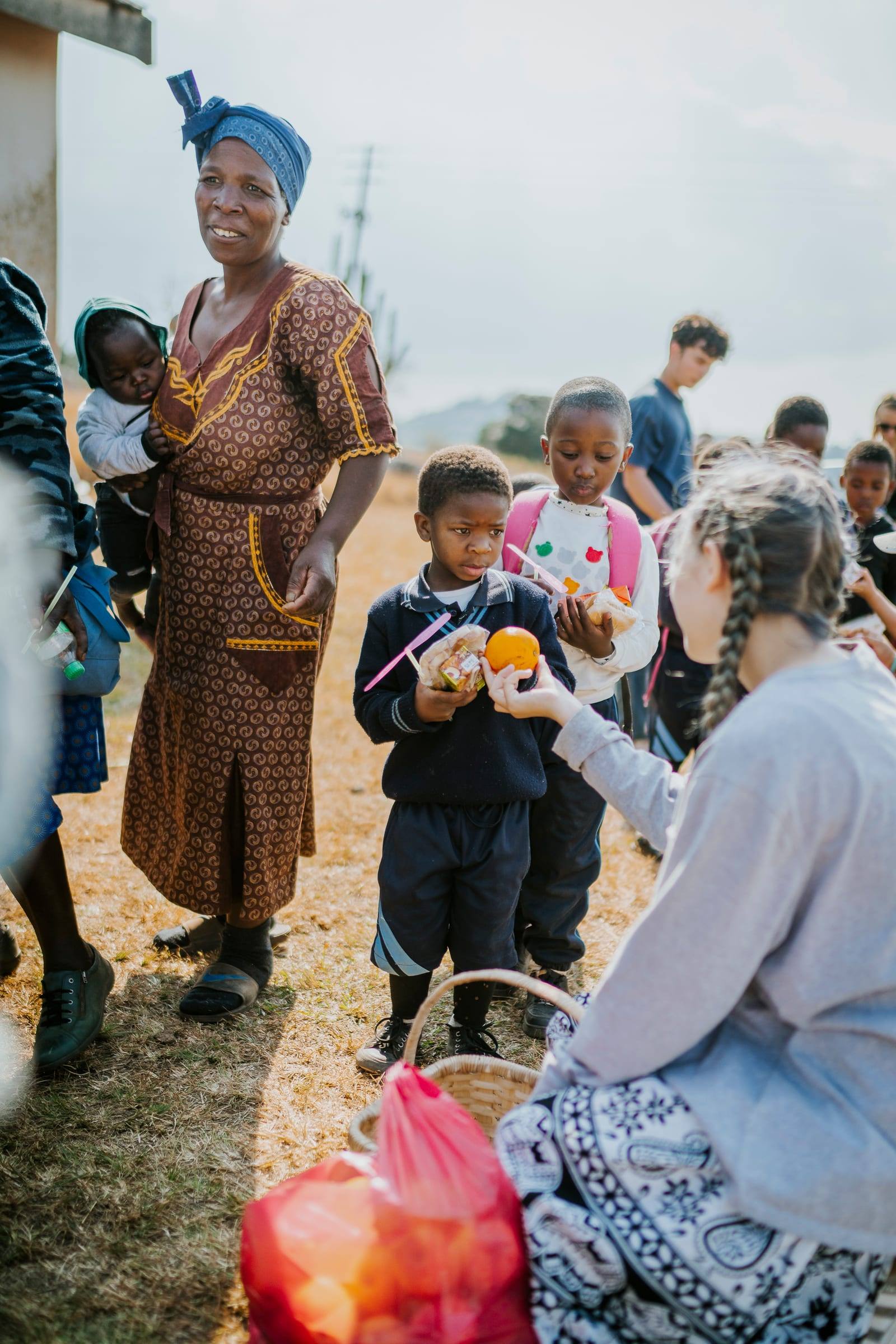 Children and a volunteer share oranges in a schoolyard
