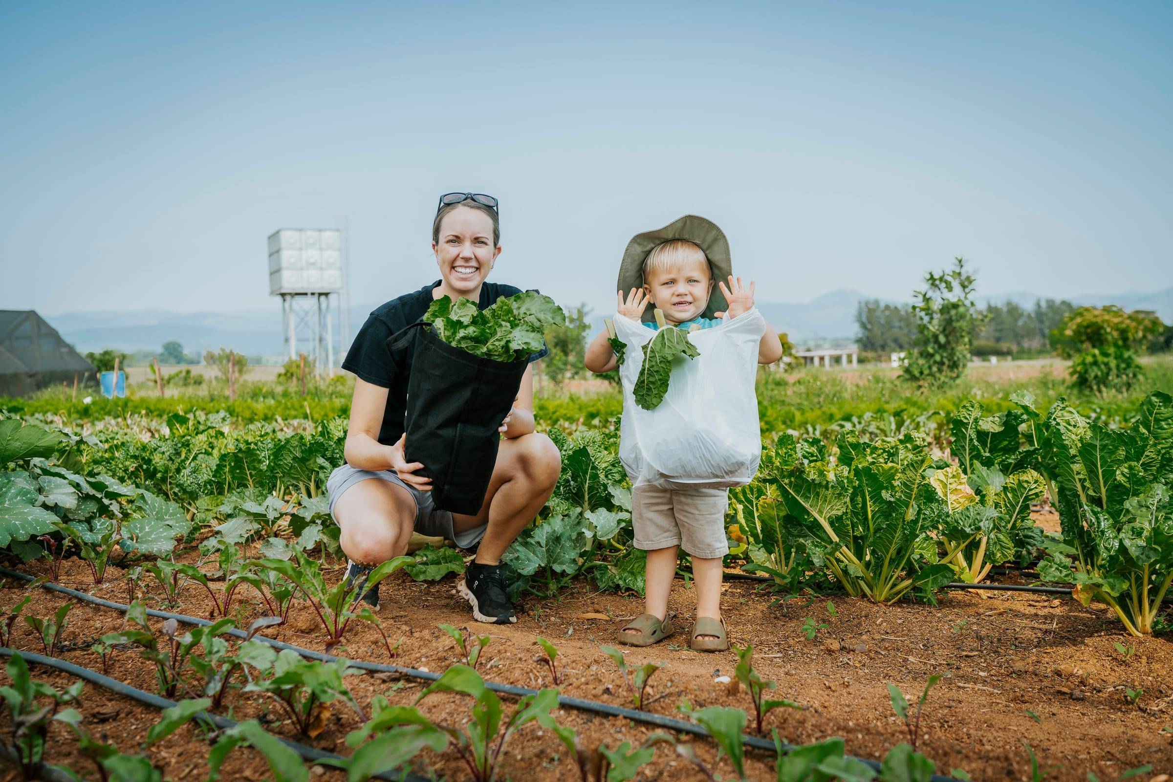 A mother and her young son hold up fresh greens from a community garden