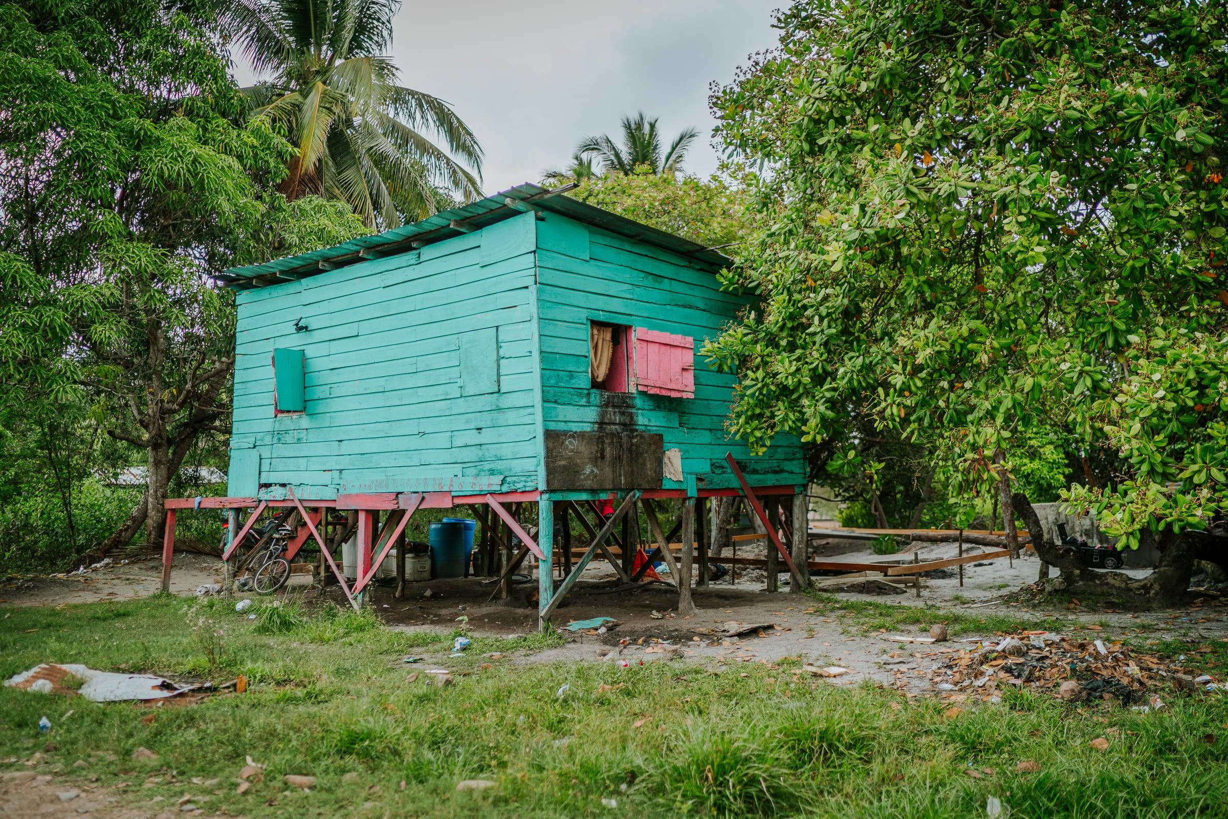 A bright teal stilt home among palm trees in Gales Point, Belize