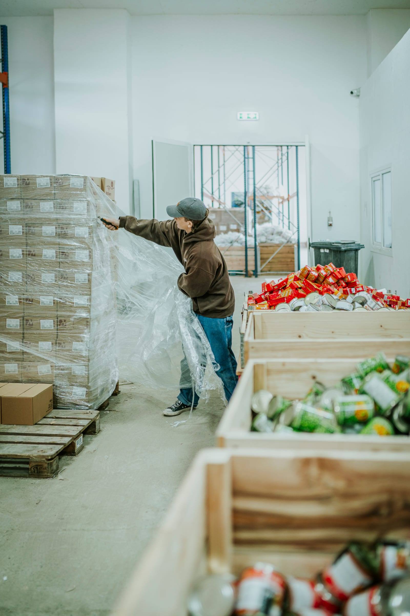 A worker wraps pallets beside crates of fresh produce