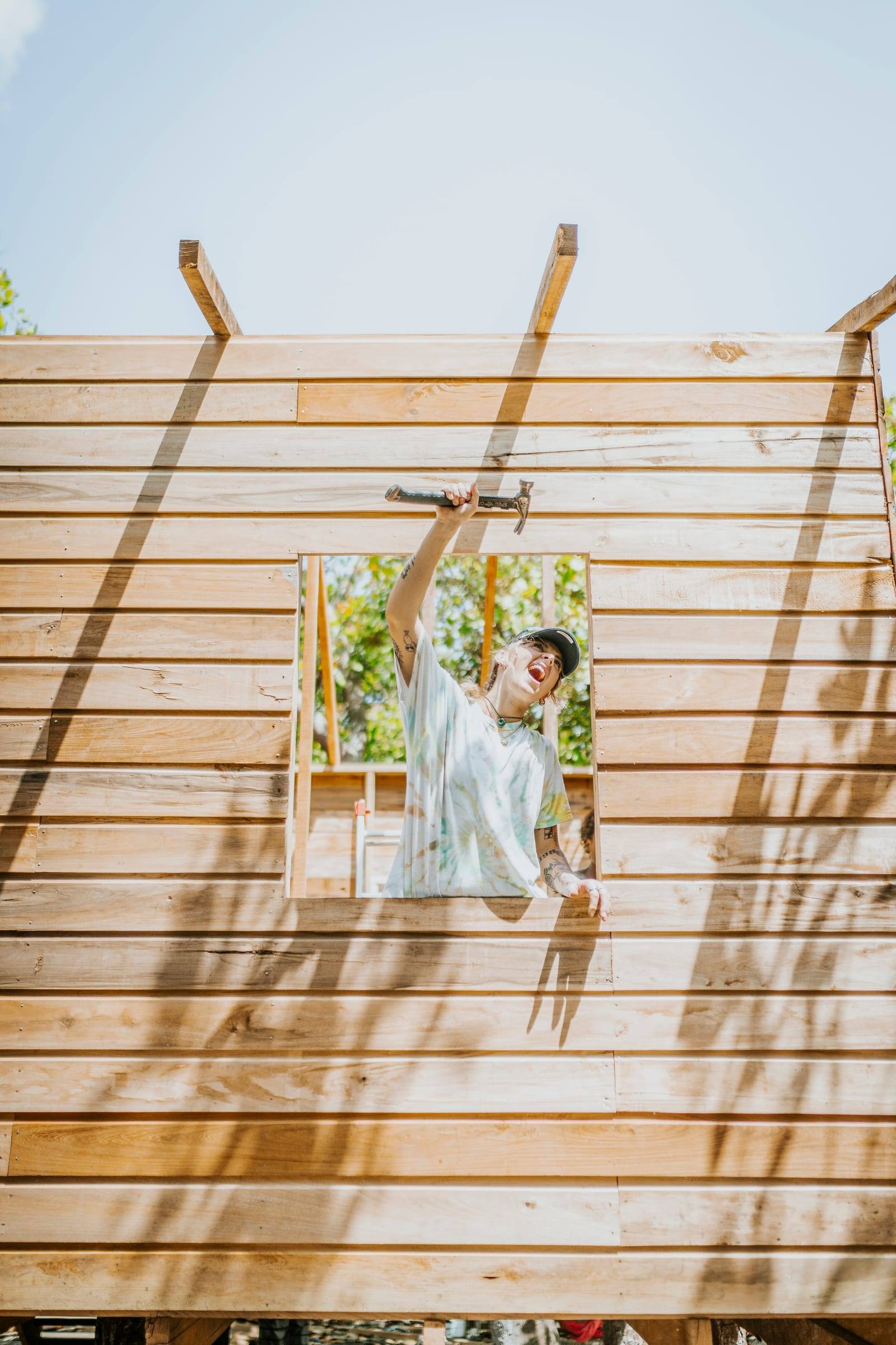 A volunteer laughs while hammering a window frame on a new home