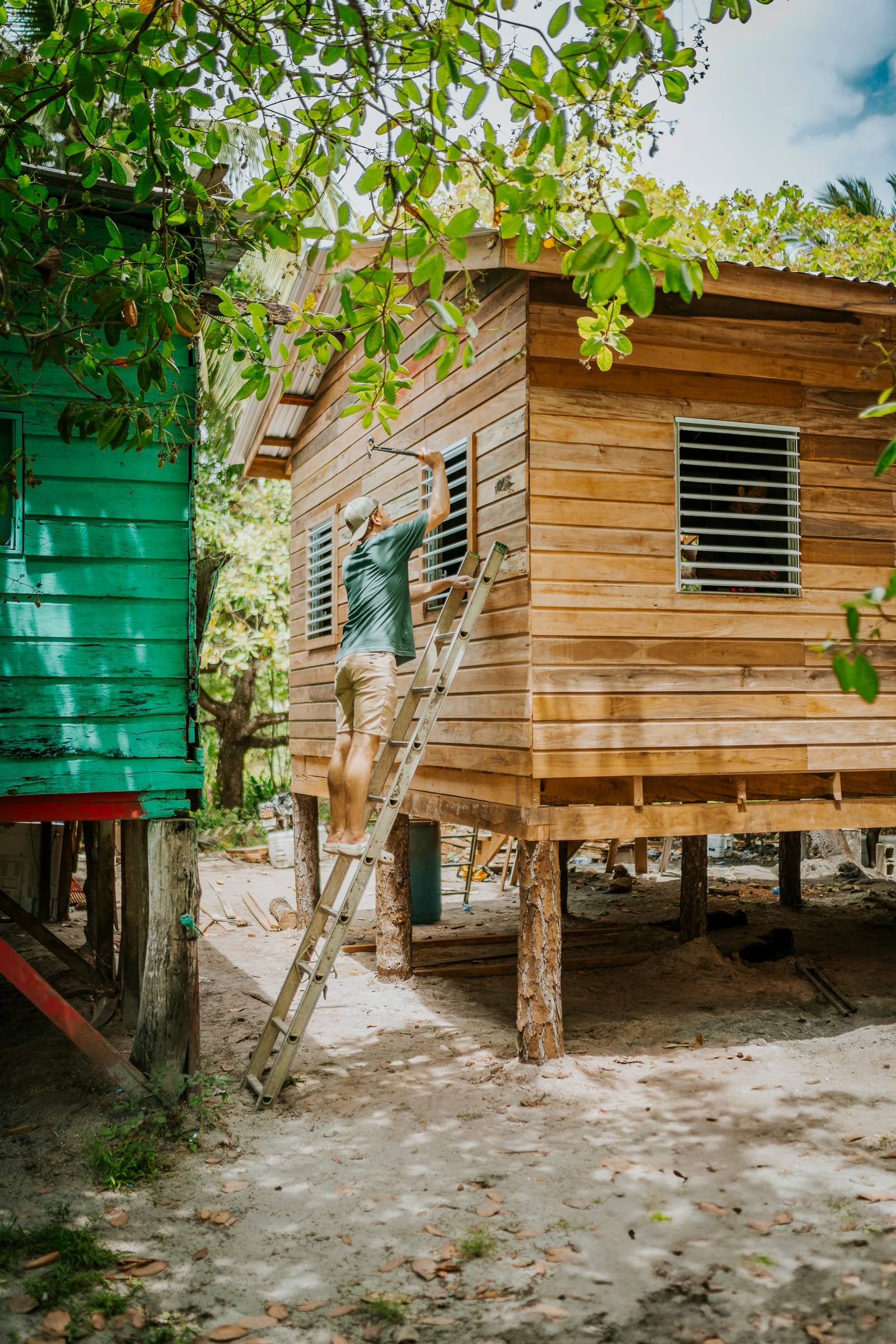 A new wooden home stands on stilts beside a bright green house