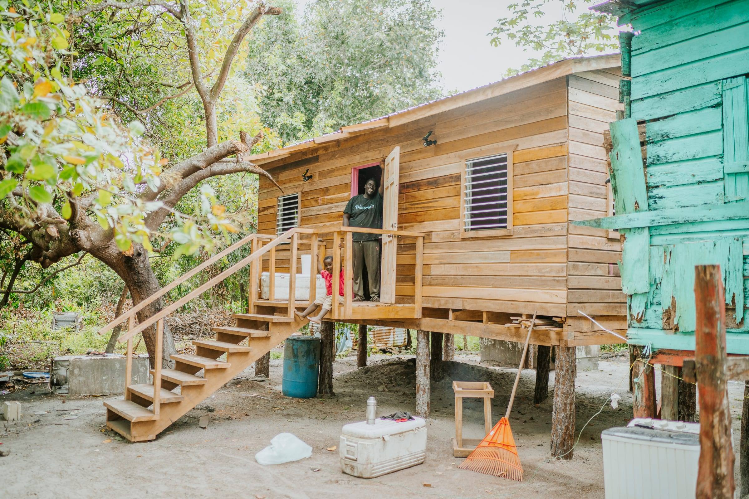 A newly built wooden stilt home with a resident in the doorway