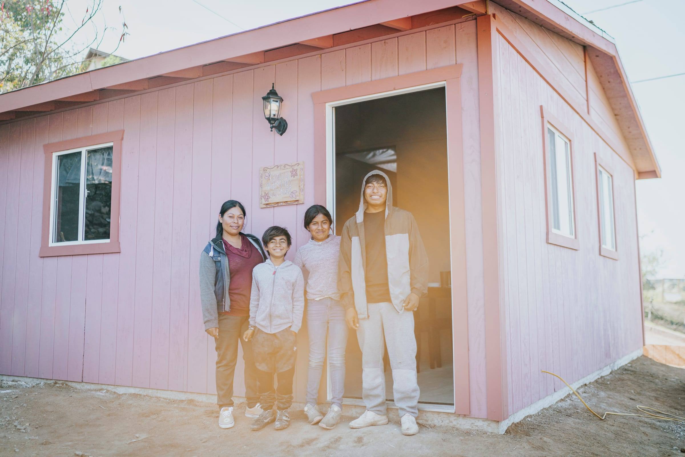 A family stands together in front of their pink home
