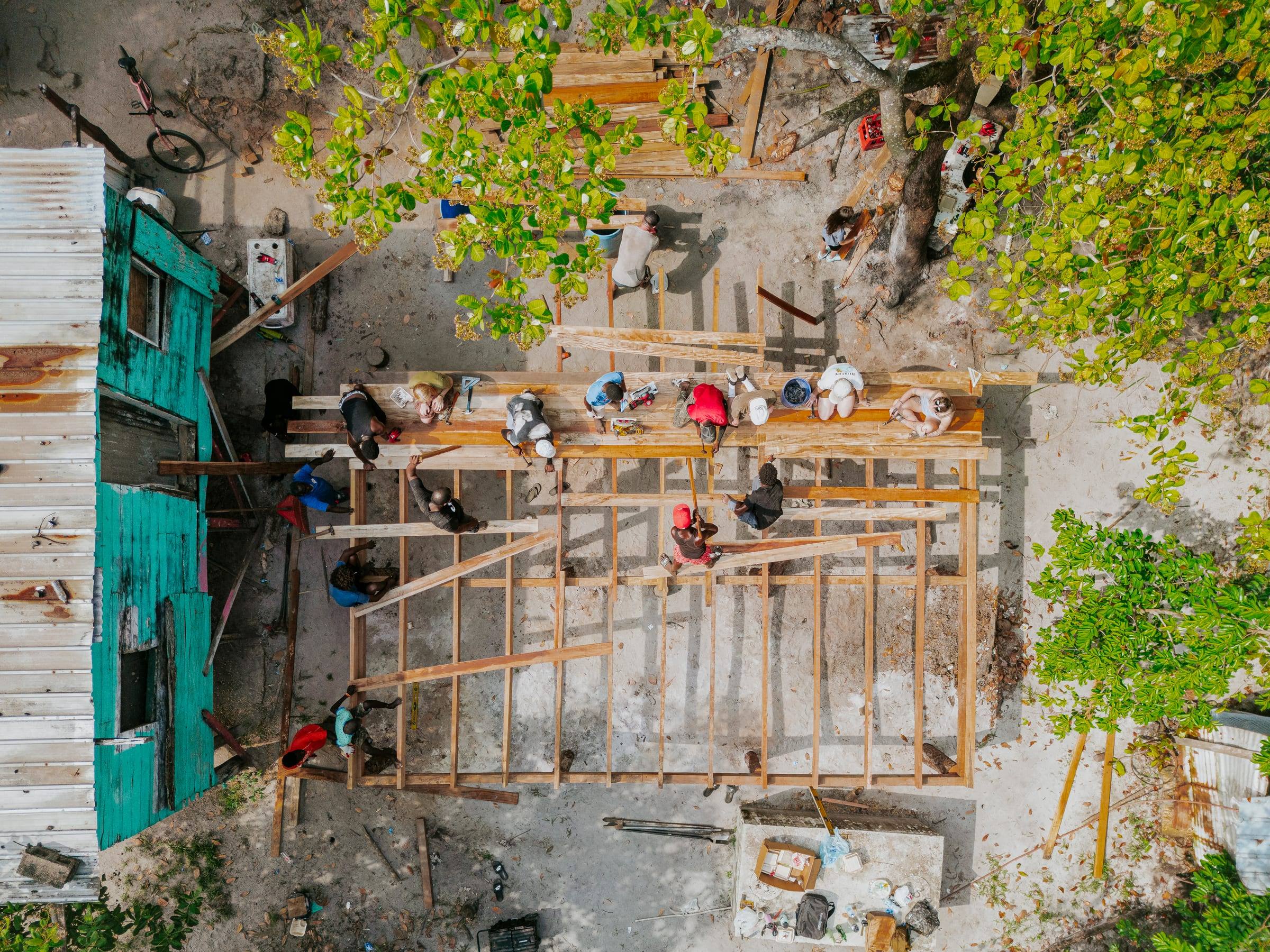 Seen from above, a team frames a new home beside a teal house among the trees