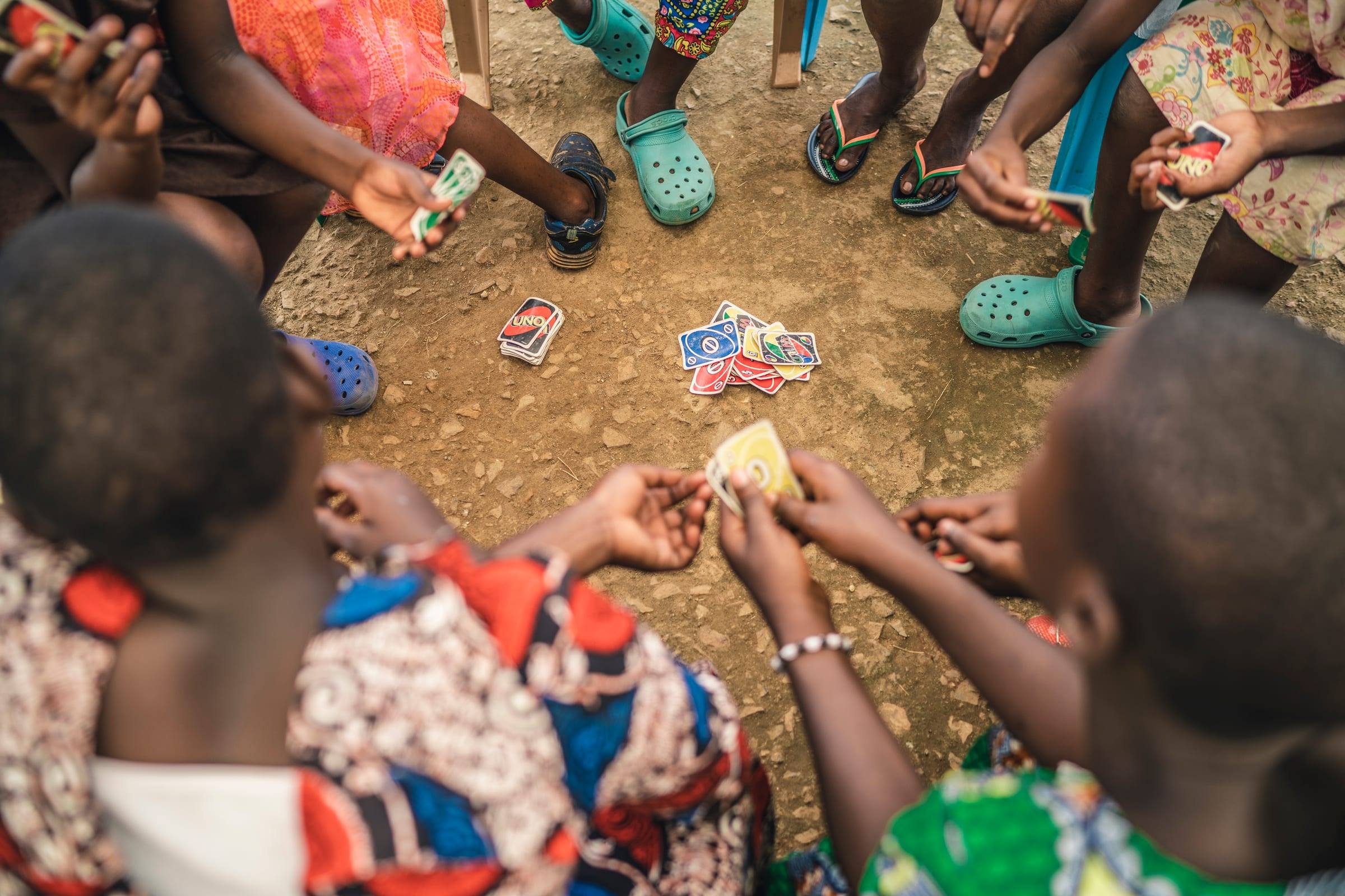 Seen from above, children play cards on red earth