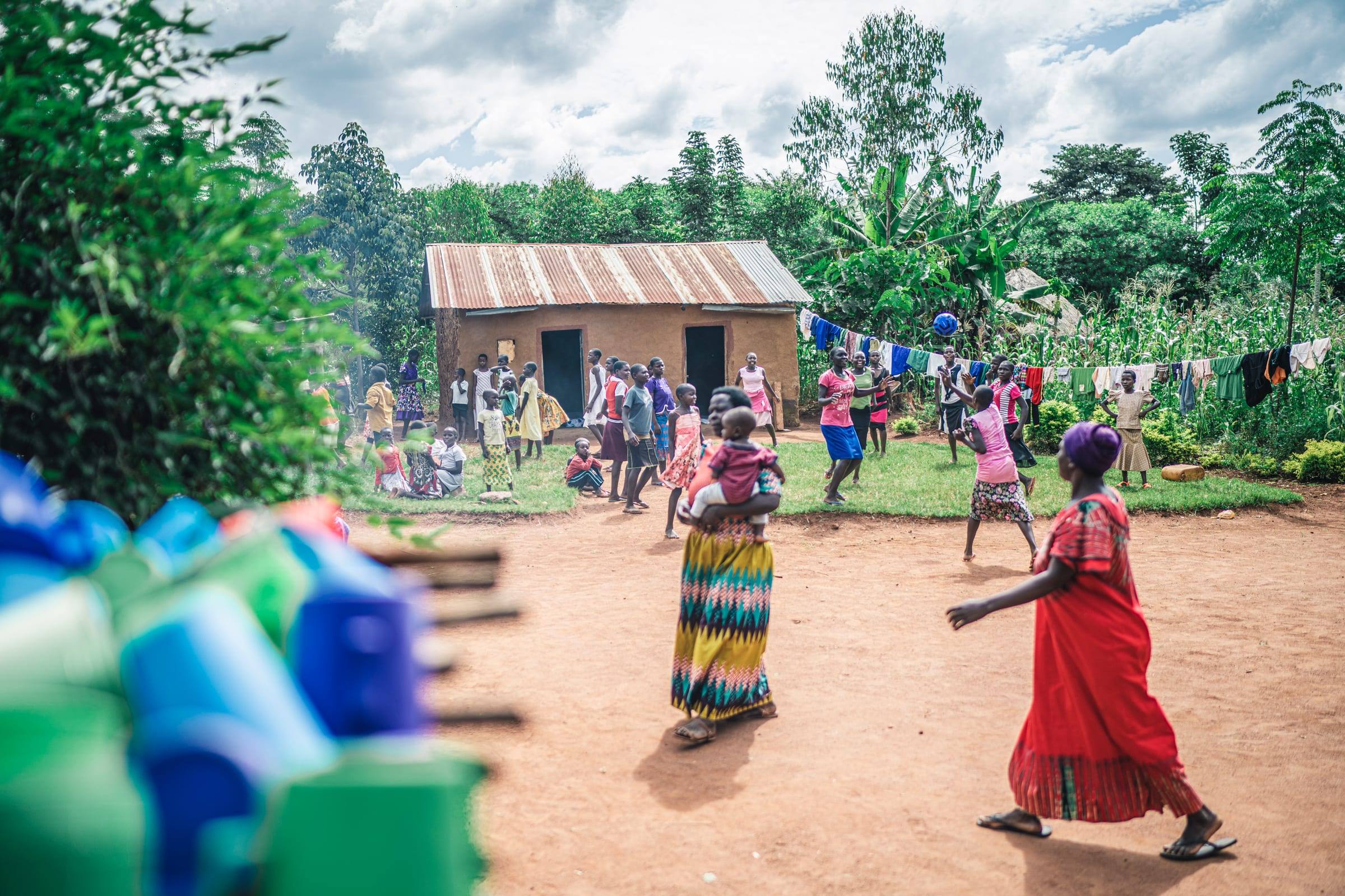 A whole community dances together in a yard beside a small house, laundry drying on the line