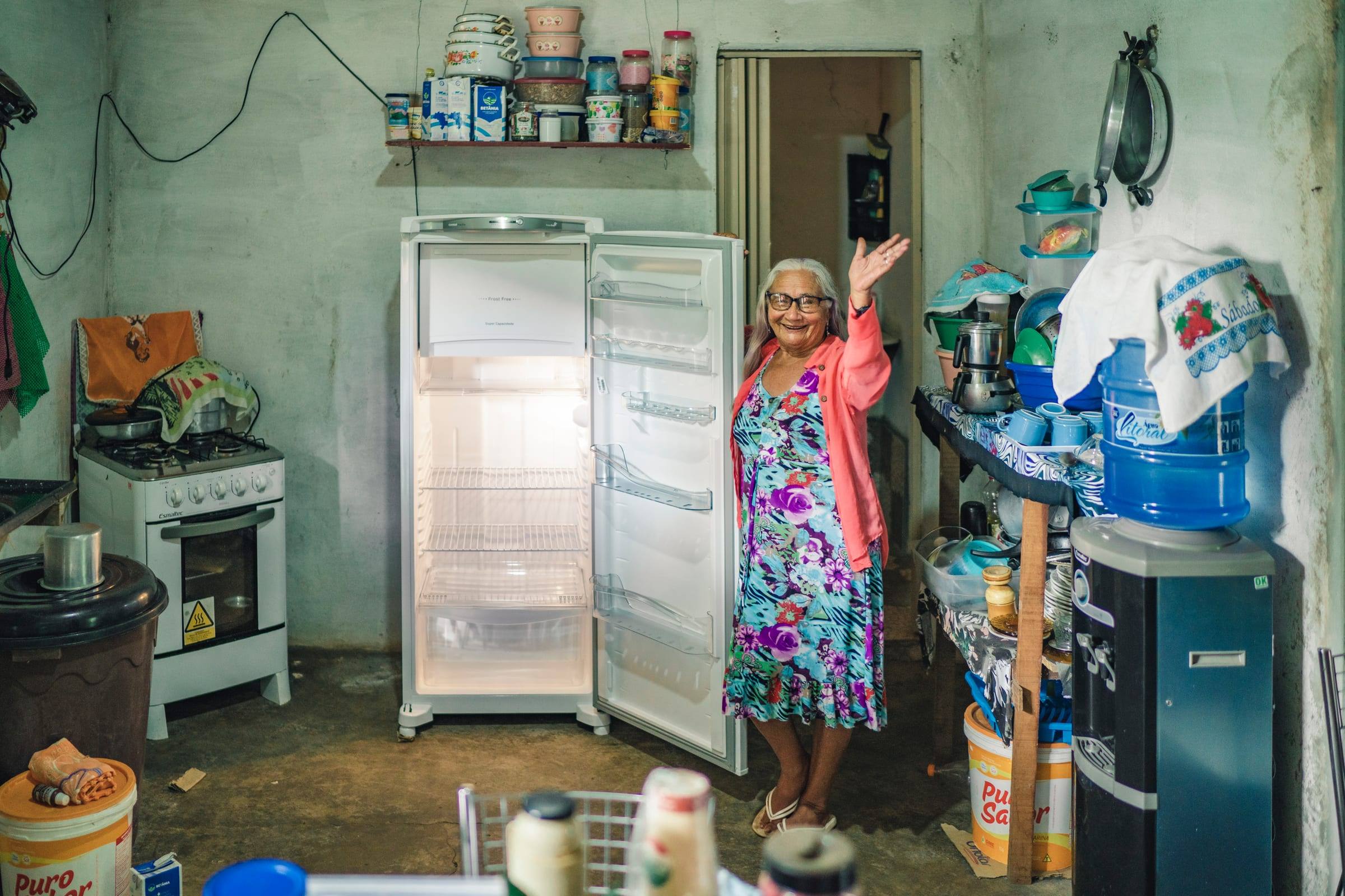 A woman smiles in her kitchen beside a refrigerator and shelves of supplies