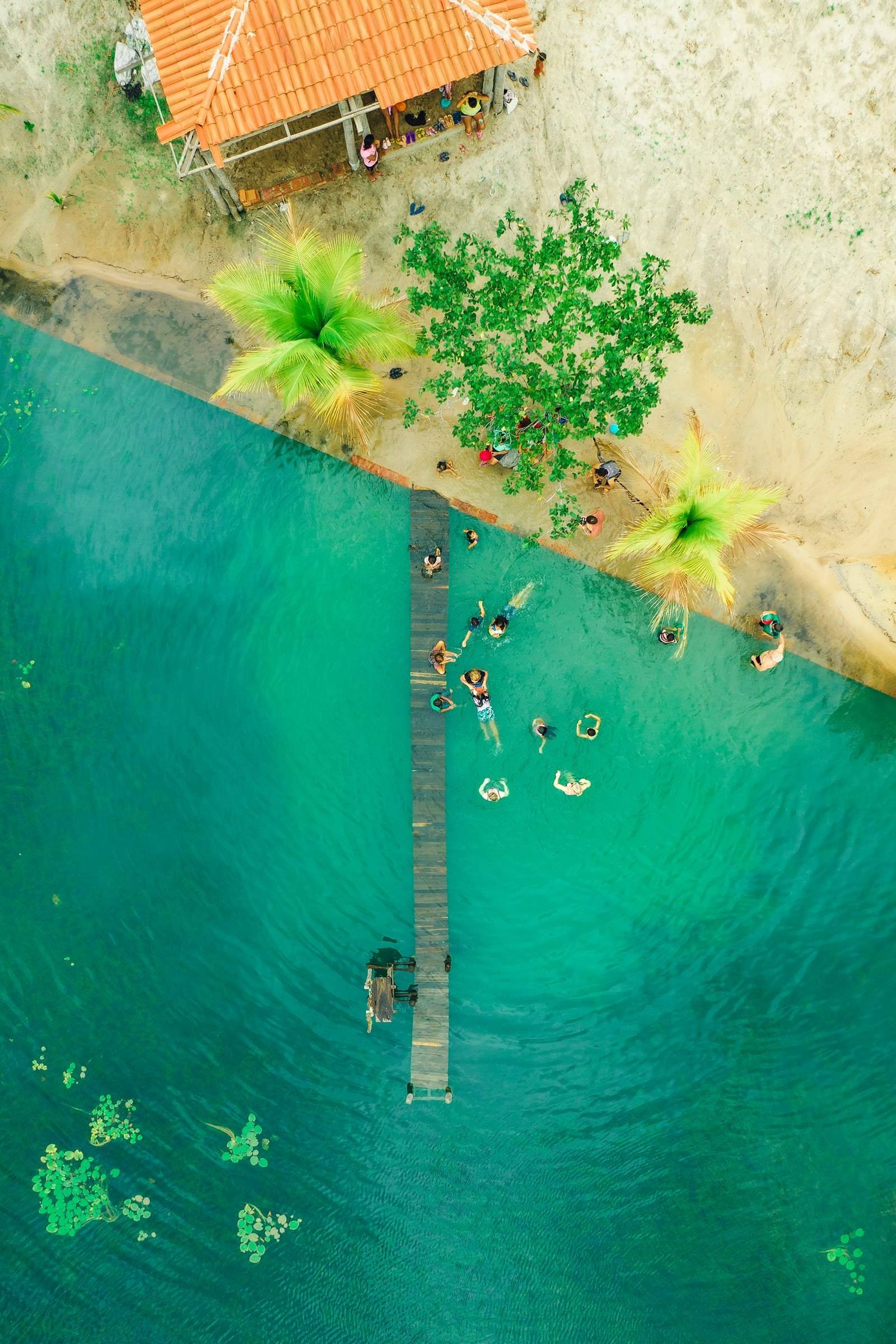 Friends swim off a wooden pier at a river swimming hole in Brazil, seen from above